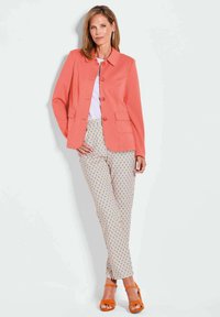 Koraalkleurige colbert met knopen, gecombineerd met gestreepte crèmekleurige broek met blauwe accenten. Draagt bijpassende oranje block-heeled sandalen.