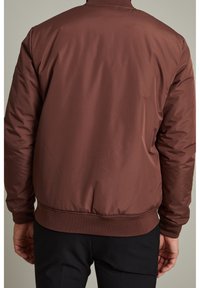 Brun vadderad bomberjacka med ribbade muddar och fåll. Slät, blank yta; inga synliga logotyper eller mönster. Visad bakifrån.