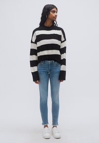 Μπλούζα πλεκτή με άσπρες και μαύρες ρίγες, στρογγυλή λαιμόκοψη, συνδυασμένη με στενά τζιν ανοιχτού μπλε χρώματος και λευκά αθλητικά παπούτσια. Η μπλούζα έχει χαμηλωμένους ώμους.