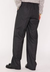 Pantaloni grigi a gamba larga realizzati in tessuto strutturato, con una cintura elastica e tasche laterali; abbinati a scarpe nere.