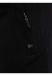 Mustast kangast lähedalt vaadatuna, millel on tõmblukuga tasku ja musta-valgete paeltega nöörid, millel on "BIG STAR" brändisilt.