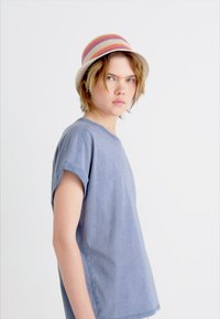 Tricou cu maneci scurte, de culoare bleu denim, cu manșete răsucite, având o croială lejeră. Asortat cu o pălărie de tip ântrusă în culori variate, cu dungi.