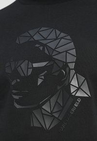 Camiseta negra con un retrato geométrico y texturizado en tonos de gris de Karl Lagerfeld, con el nombre impreso en la parte inferior.