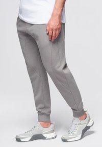 Ljusgrå träningbyxor med tapered fit som har bågformade sömmar, parat med grå och vita träningsskor med texturerade detaljer.