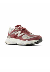 Zapatilla atlética roja y gris con materiales de malla y ante, prominente logo "N", entresuela blanca acolchada y suela negra texturizada.