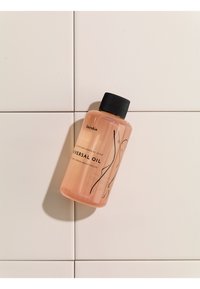 Pink plastic bottle labeled "Universal Oil," featuring a black screw cap and minimal line design. Positioned on white tiled surface.