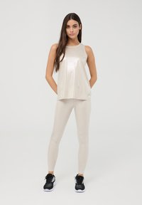 Top senza maniche beige chiaro e leggings abbinati con una finitura metallizzata brillante. L'outfit include scarpe sportive nere.