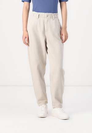 Pantaloni bej deschis, lejere, cu talie elastică, buzunare frontale și un material ușor texturat. Asortați cu adidași albi.