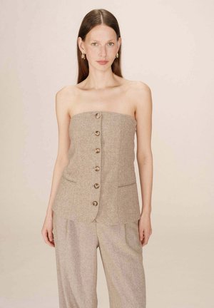 Haut beige sans bretelles en tissu texturé, avec une fermeture centrale à bouton, des poches latérales et des coutures discrètes pour un look ajusté.