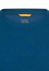 T-shirt en coton bleu avec un col rond, présentant un petit accent orange au niveau du col et un logo imprimé à l'intérieur du col.