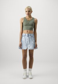 Lyseblå denimskjørt med hvitt blomstermønster, høy midje-design, kombinert med en tettsittende olivengrønn crop top og hvite joggesko.