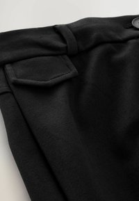 Schwarzer Stoff mit einer flachen Tasche und einem Knopfdetail, das eine glatte Textur und ein strukturiertes Design in einer Nahaufnahme zeigt.