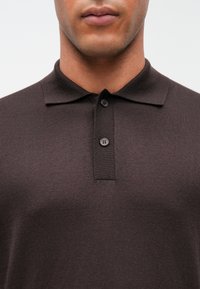 Mørkebrun polo skjorte med strukturert strikket stoff, tre knapper i kragen, og en klassisk silhuett.