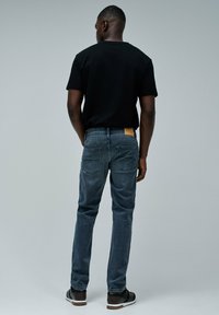 Jeans de mezclilla oscura con un corte recto, combinados con una camisa negra de manga corta. Presentan una etiqueta de cuero en la parte posterior de la cinturilla y bolsillos traseros inclinados.