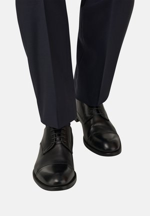 Schwarze Leder-Businessschuhe mit abgerundeten Zehen, Schnürsenkeln und glatter Oberfläche, kombiniert mit einer navyblauen Hose mit einer Bügelfalte.