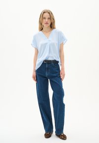 Blusa corta a maniche corte di colore azzurro chiaro con scollatura a V, abbinata a jeans dritti a vita alta di colore blu scuro e ballerine in stampa leopardata marrone.