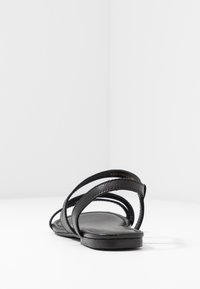 Sandale plate noire avec plusieurs fines lanières et semelle rembourrée, photographiée de l'arrière sur fond blanc.