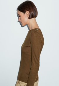 Brown long-sleeve sweater with a round neckline, featuring a button accent on the shoulder and a fitted design. Smooth texture.