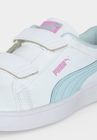 Λευκό αθλητικό παπούτσι Puma με ανοιχτό μπλε πλαϊνή ρίγα, ροζ λογότυπα Puma και δύο λευκές λουριά με βέλκρο.