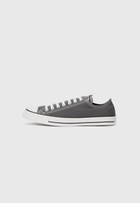 Gray canvas sneaker with white rubber sole, white laces, and toe cap. Features stitching accents and a small logo tag on the heel.