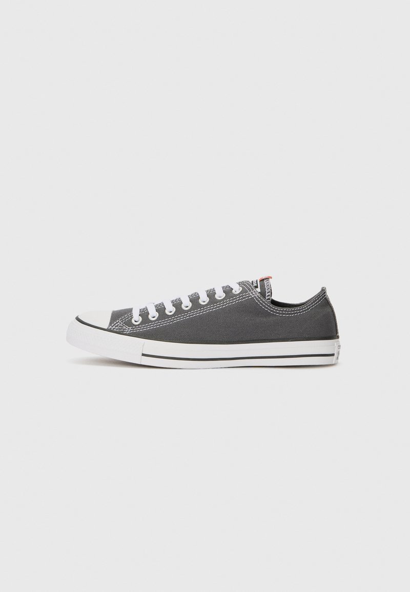 Gray canvas sneaker with white rubber sole, white laces, and toe cap. Features stitching accents and a small logo tag on the heel.