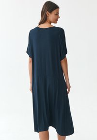 Laivastonsininen polvipituinen mekko, jossa on rento istuvuus, leveät hihat ja sileä pinta. Yksityiskohtana sauman kohta vyötäröllä.
