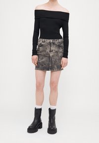 Czarny prążkowany top typu off shoulder, szara spódnica dżinsowa w gwiazdy oraz czarne masywne botki za kostkę z grubą podeszwą i detalami na zamek.