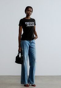 Svart t-skjorte med "DKNY JEANS" i rhinestones, kombinert med lyseblå vide jeans med slitte detaljer. Tilbehør med en liten svart veske.