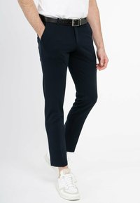 Marineblaue, taillierte Hosen mit slim fit, flachem Bund, seitlichen Taschen und einem schwarzen Gürtel. Kombiniert mit weißen Sneakers.