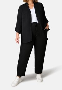 Svart långärmad skjorta med knäppning och två bröstfickor, kombinerad med svarta byxor med dragsko och vita sneakers.