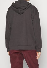 Felpa con cappuccio grigia scuro, dal taglio ampio, con orlo a coste e maniche a sbuffo. Indossata con pantaloni in velluto a coste bordeaux.