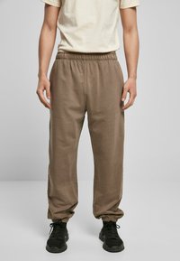Brune, lette joggebukser med elastisk midje og smalning ved anklene, kombinert med en ensfarget lyse T-skjorte og svarte joggesko.