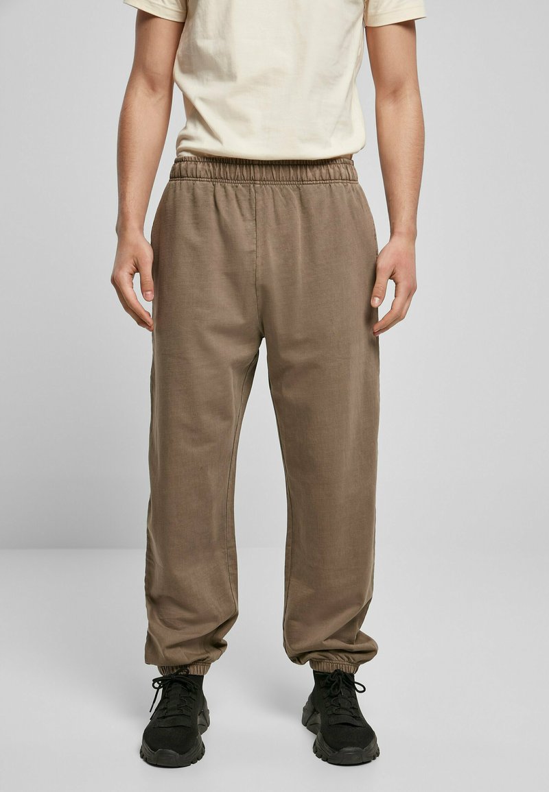 Brune, lette joggebukser med elastisk midje og smalning ved anklene, kombinert med en ensfarget lyse T-skjorte og svarte joggesko.