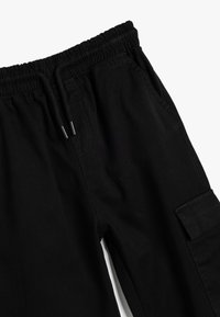 Pantaloni cargo neri con vita elasticizzata e cordoncino, tasche laterali e tessuto testurizzato. Il design include una tasca applicata su una gamba.