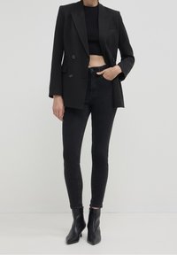 Blazer noir cintré avec deux boutons à l'avant, associé à un haut noir court et un jean skinny noir. Porté avec des bottines noires à talons pointus.