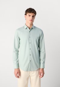 Cămașă cu mânecă lungă din țesătură verde deschis, cu deschidere cu butoane pe față și butoane gri, având un guler și mansete clasice, textură netedă.
