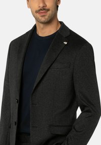 Dunkelgrauer Blazer mit feiner Textur, einreihigem Design, Reverskragen und Brusttasche. Getragen über einem navyblauen Rundhalshemd.