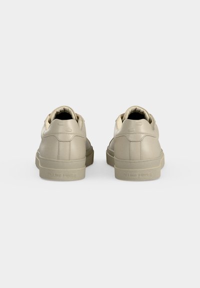Ζευγάρι μπεζ δερμάτινα sneakers χαμηλού ύψους εμφανίζονται από πίσω σε απλό ανοιχτό γκρι φόντο.