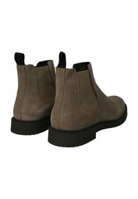 Par de botas Chelsea de ante en color topo con paneles laterales elásticos negros y tiradores negros, que presentan suelas de goma negra gruesas.