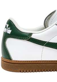 Witte leren sneaker met groene accenten, textuur rubberen zool en gestikte details. Heeft een logo op de hiel en een gevoerde kraag.