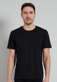 Black crew-neck t-shirt made of cotton, featuring short sleeves and a small embossed logo on the left chest area. Smooth texture.