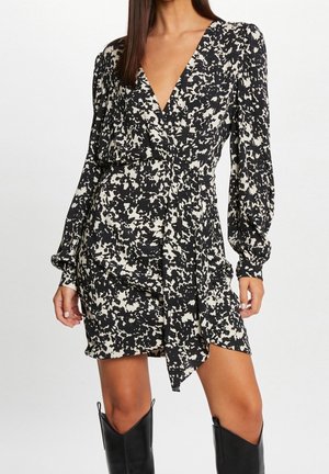 Robe portefeuille noire et crème à imprimé floral, manches longues bouffantes, décolleté en V profond, et taille nouée, assortie à des bottes noires montantes jusqu'aux genoux.