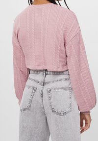Maglione corto lavorato a maglia di colore rosa con motivo a treccia, maniche lunghe e texture a coste. Abbinato a jeans in denim grigi a vita alta con tasche.