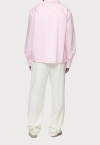 Różowa, w paski, longsleeve z luźnym fasonem i detalem w postaci yoke z tyłu, w połączeniu z białymi spodniami z szerokimi nogawkami i jasnymi butami.