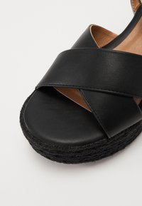 Schwarze Ledersandale mit kreuzenden Riemen, offenem Zehenbereich und einer strukturierten schwarzen Plattformsohle. Das Innere verfügt über eine glatte, beige Innenausstattung.