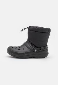 Botte noire en caoutchouc avec une tige rembourrée, dotée d'un système de fermeture par cordon, de trous d'aération et d'une semelle texturée.