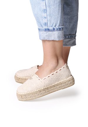 Cream-colored espadrilles with a crocheted upper, scalloped edge, and braided jute sole. Worn with rolled denim trousers.