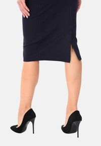 Scarpe nere in suede con tacco alto, dalla punta affusolata e un design a taglio nella parte anteriore. Tacchi a spillo sottili che esaltano il design.