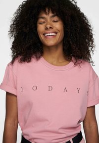 T-shirt in cotone rosa con maniche corte e risvolti, con la scritta "1 0 D A Y S" in nero, scollatura rotonda, vestibilità rilassata.