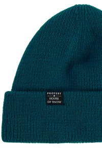 Tyrkysová pletená čepice s ribbed texturou. Na okraji je umístěna černá etiketa s bílým textem "PROTEST HOUSE OF SNOW", která je přišitá.